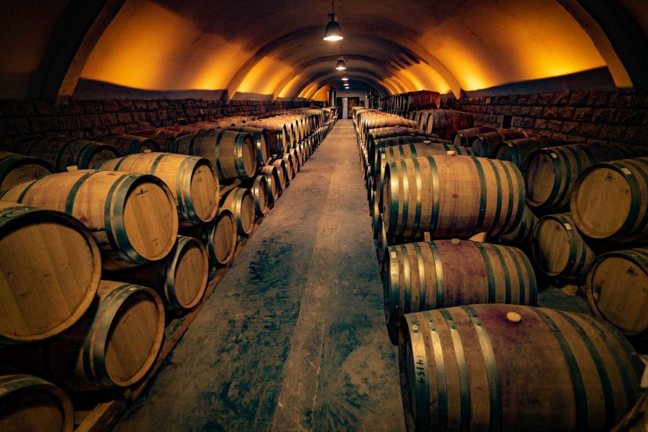 Imagem com fundo infinito mostrando diversos barris de madeira, empilhados no processo de envelhecimento do vinho.