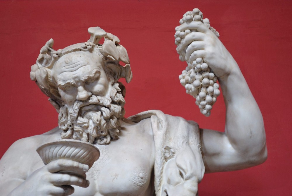 Estátua de Dionísio com uma taça de vinho na mão direita e um cacho de uvas na mão esquerda. 
