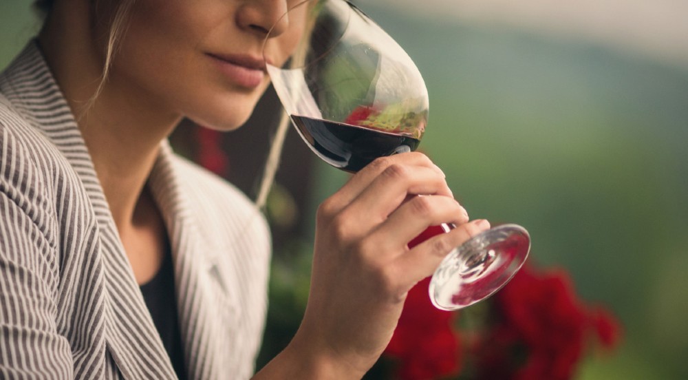 Mulher segurando uma taça de vinho tinto e cheirando o conteúdo para conhecer mais sobre o sabor