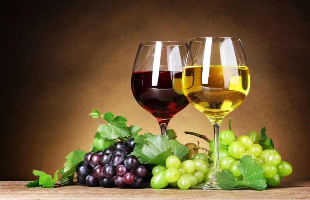 Duas taças de vinho branco e vinho tinto, uma ao lado da outra, envoltos por uvas brancas e tintas.