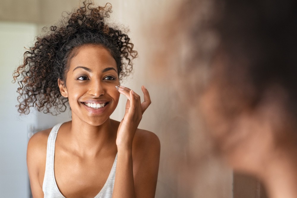 Mulher da pele preta se olhando no espelho e feliz com os resultados da sua pele