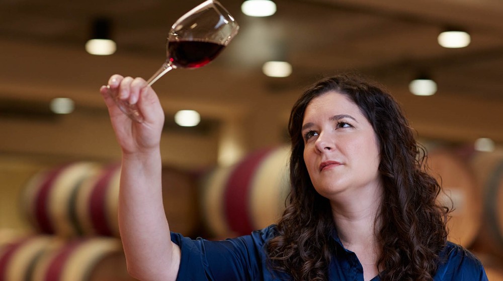Enóloga ergue uma taça de vinho tinto enquanto analisa seu conteúdo.