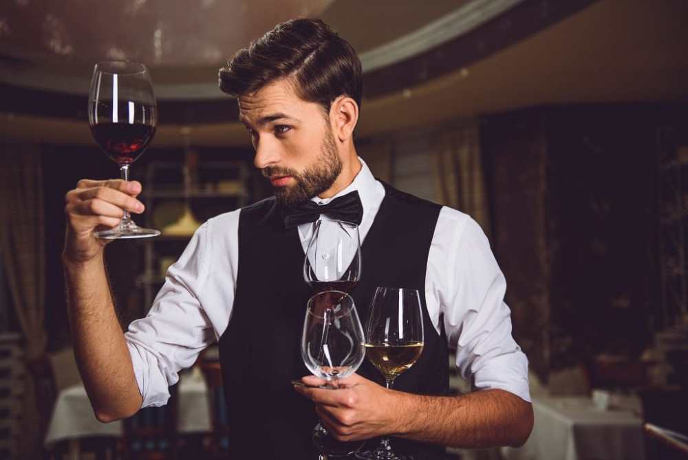 Sommelier analisando um vinho tinto enquanto segura outras duas taças de vinho.