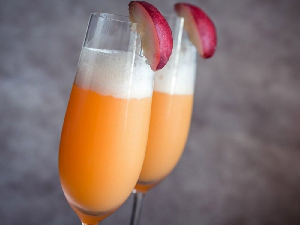 Duas taças de vidro com drink bellini enfeitadas com um pedaço de pêssego